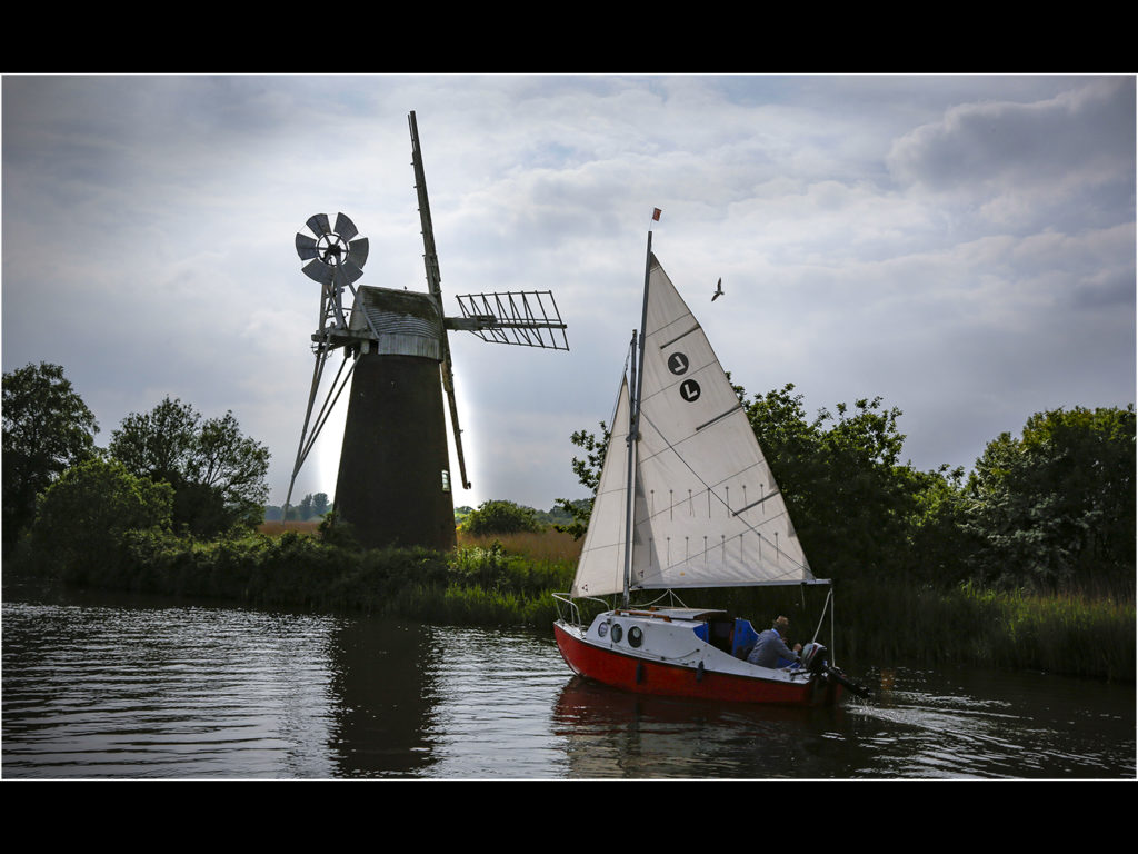 an image of a sail boat on the Norfolk Broads near a windmill